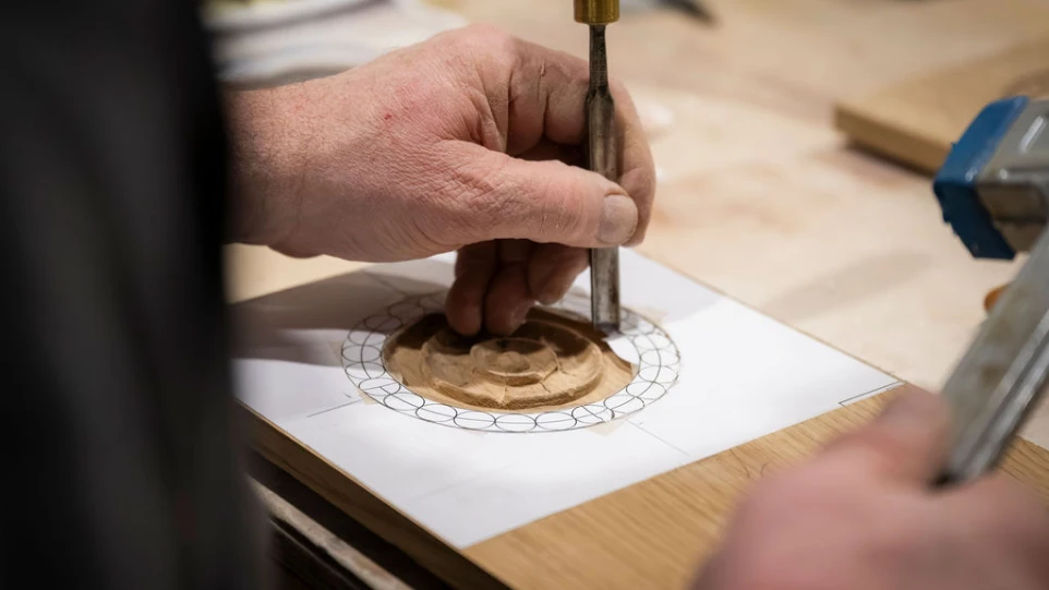 Un menuisier qui sculpte du bois massif pour une porte d'entrée bruxelloise à l'identique